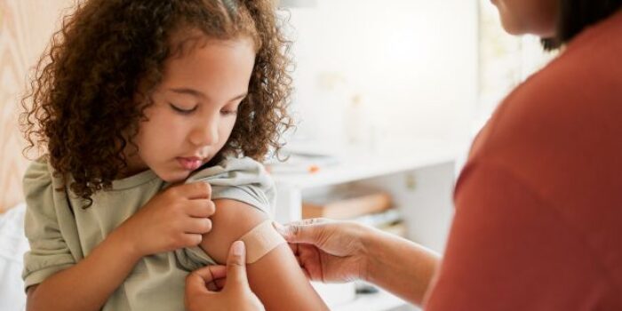 Young girl looking at plaster on arm after vaccination