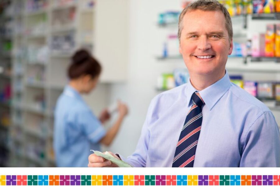 Male pharmacist smiling at camera holding prescription